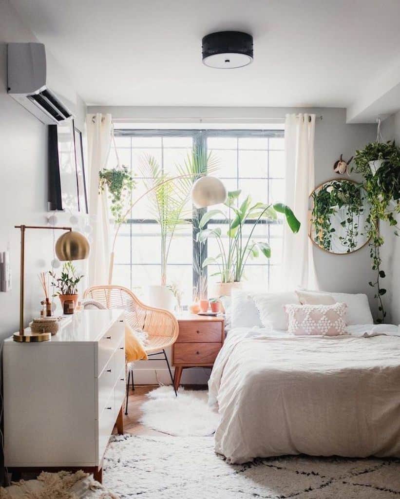 Boho bedroom with abundant plants, white dresser, and gold accent lamps.