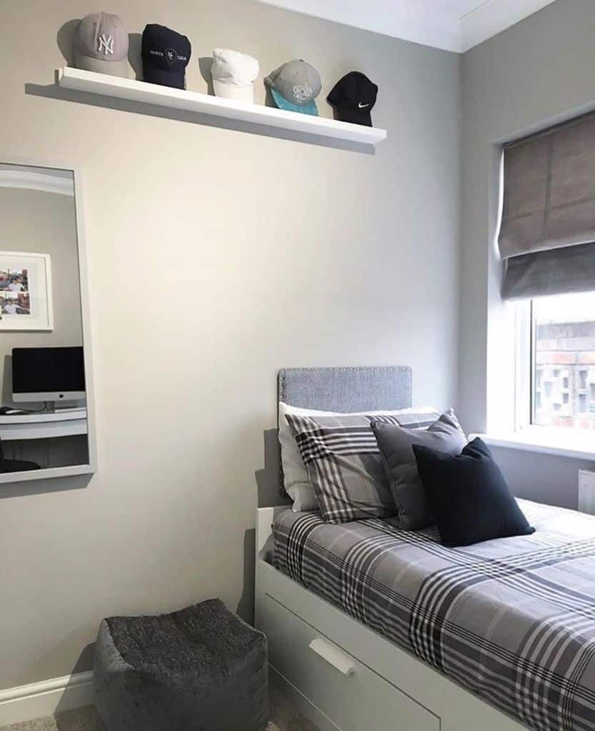 Gray bedroom with plaid bedding, wall-mounted hat shelf, and a window with blinds.