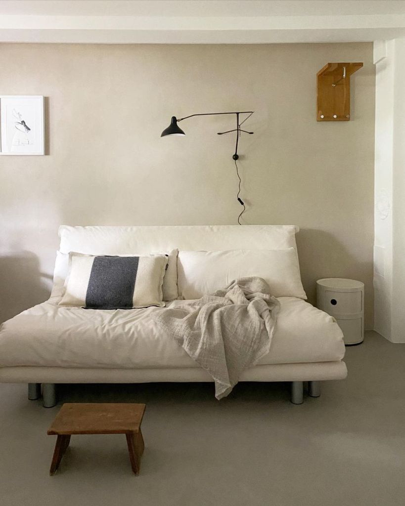 Minimalist bedroom with cream sofa bed, wall-mounted lamp, and neutral decor.