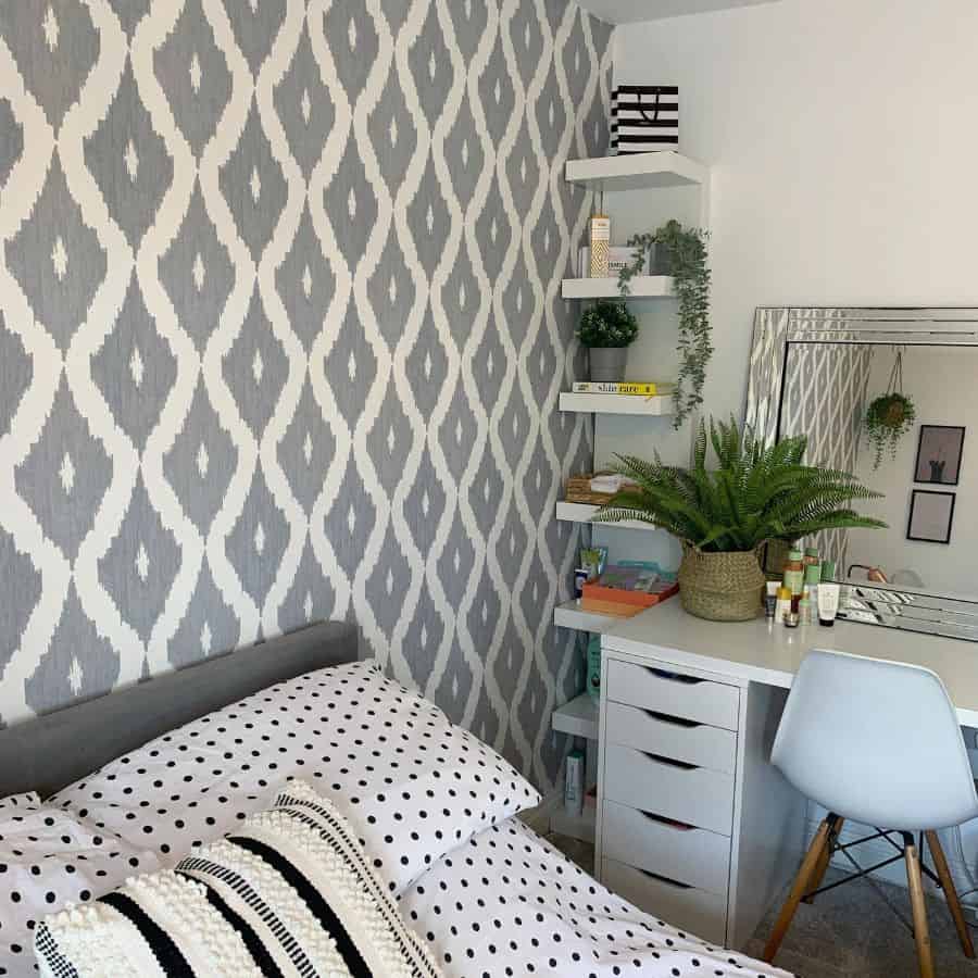 Bedroom with patterned wallpaper, white desk, plants, and floating shelves.