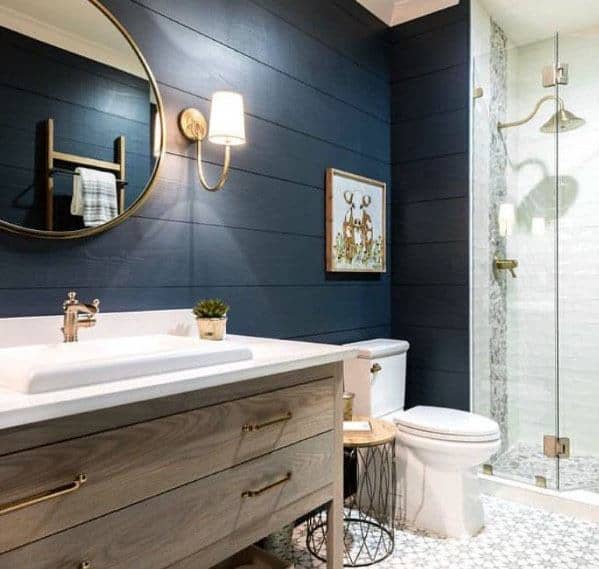 Bathroom with navy shiplap walls, wood vanity, round mirror, and glass shower.