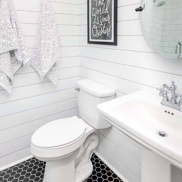 Charming half-bath with white shiplap walls, black hexagon tile flooring, and vintage fixtures.