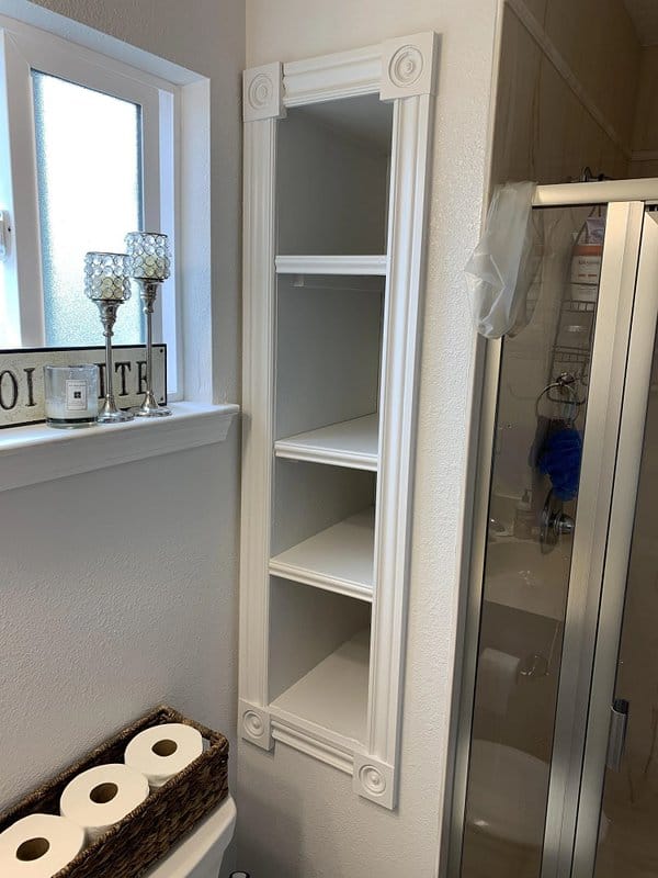 White built-in shelving unit in a bathroom corner, ideal for storage, with decorative accents and a window nearby