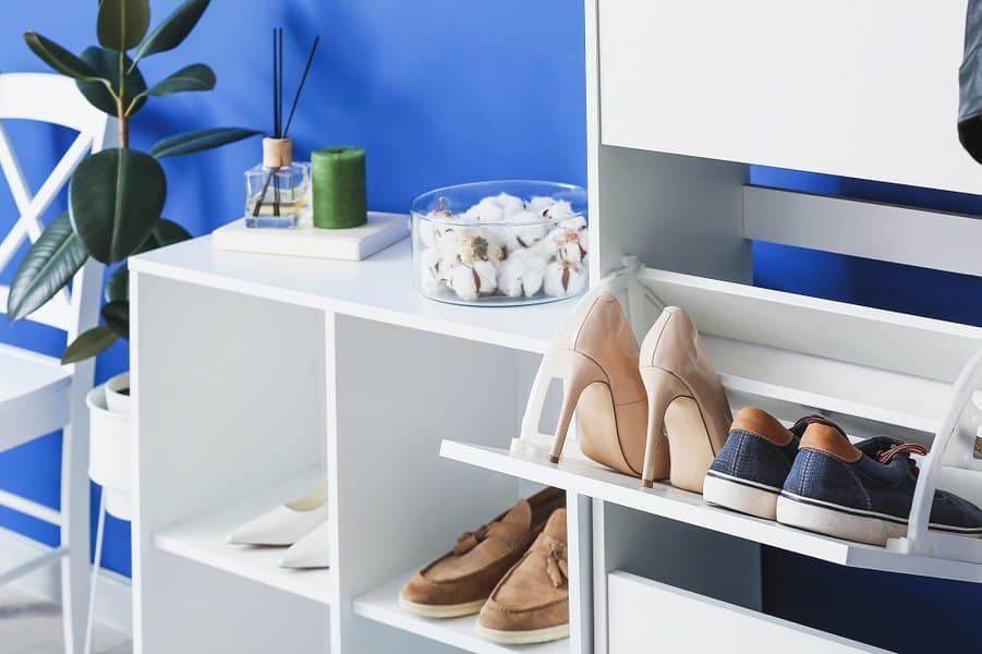 White shoe storage unit with open cubbies and pull-out compartments, holding a mix of sneakers and heels, set against a blue wall