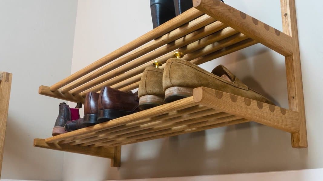 Wall-mounted wooden shoe rack with slatted shelves, neatly holding dress shoes and boots in a compact and elegant design