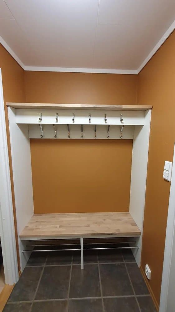 Entryway storage bench with a wooden top, built-in shoe rack, and wall hooks, set against a warm orange accent wall