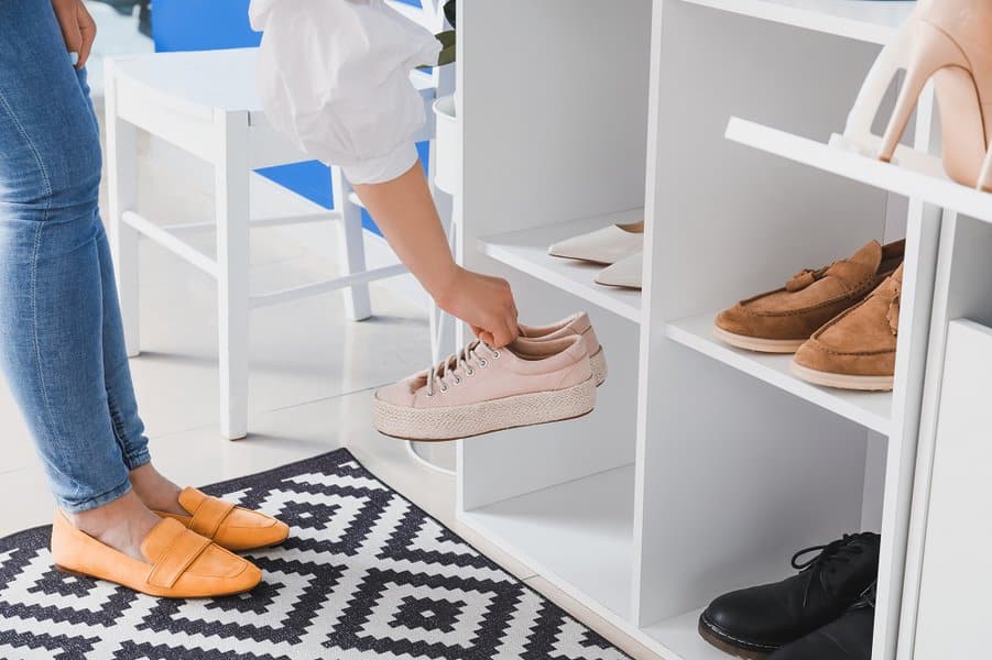 White cubby-style shoe organizer holding various shoes, with a person placing pink sneakers inside on a geometric-patterned rug