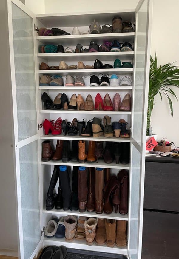 Tall white shoe cabinet with glass doors, organizing various types of shoes and boots across multiple shelves in a neat layout