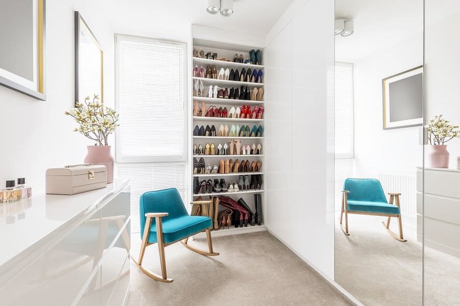 Modern walk-in closet with a tall built-in shoe rack showcasing colorful heels and flats, complemented by a teal accent chair