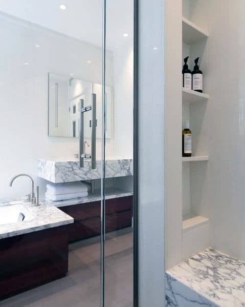 Modern bathroom with marble countertop, glass shower door, and built-in wall shelving.