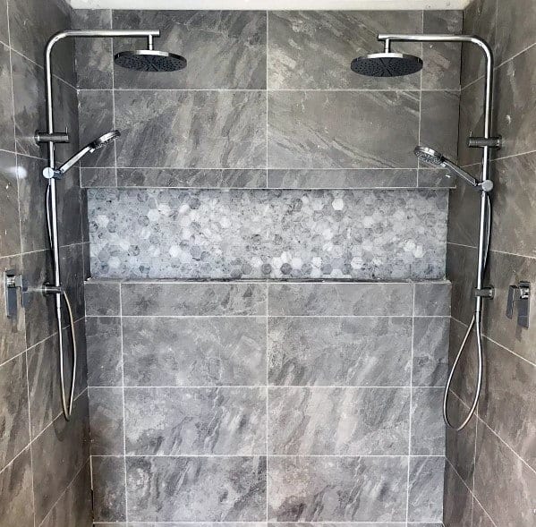 Double shower heads with gray marble tiles and hexagonal accent niche.