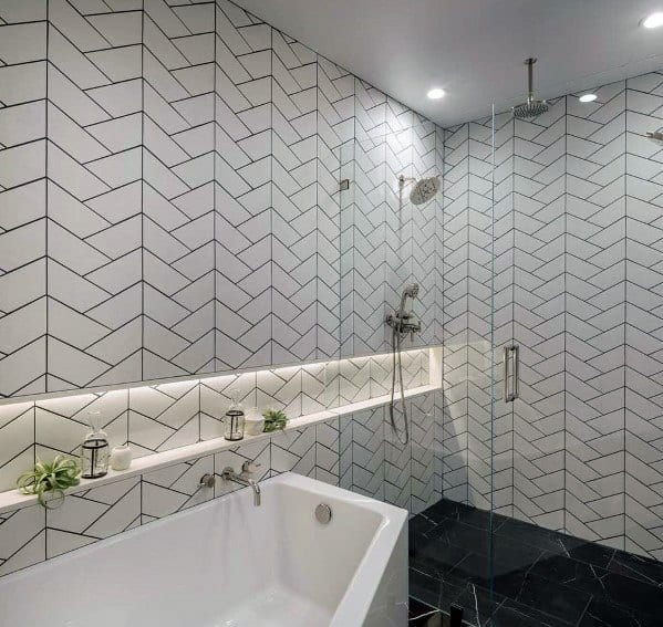 Bathroom with white herringbone tiles, glass shower, built-in illuminated shelf, and bathtub.