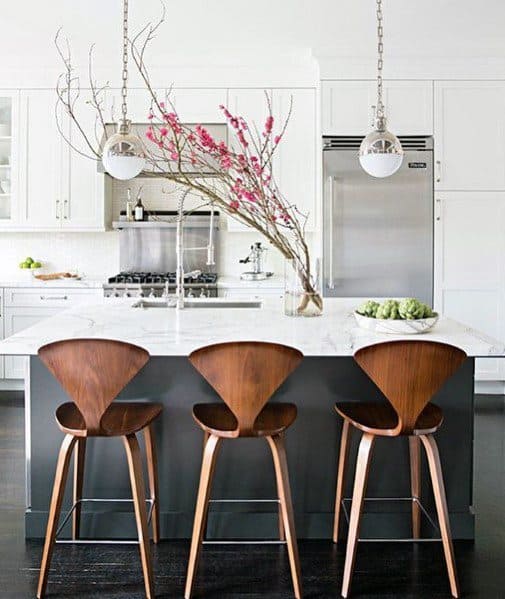 Stylish kitchen with silver and white pendant lights above a white marble island, complemented by modern wooden bar stools and minimalist decor