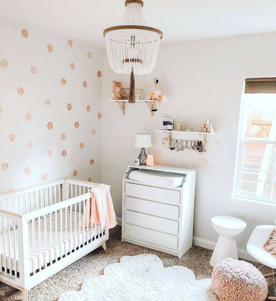 Nursery with pink circle wallpaper, white crib, changing table, and boho chandelier.