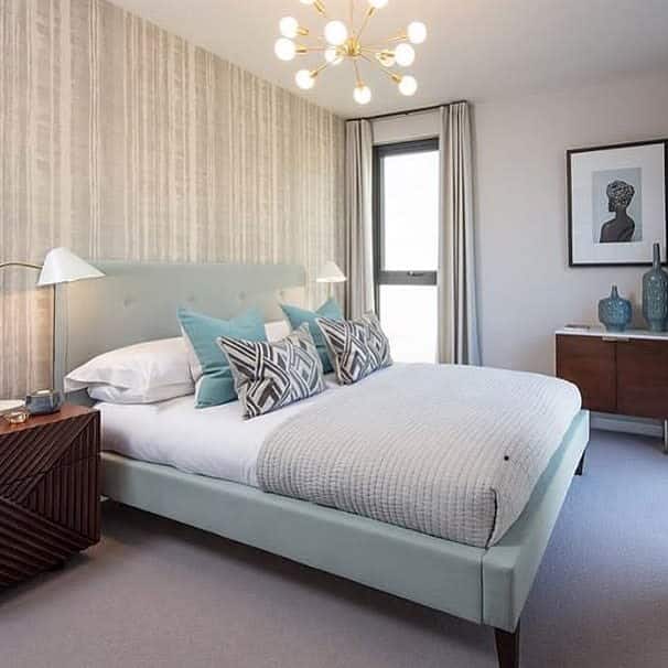 Modern bedroom with textured gray wallpaper, pastel bed, and geometric throw pillows.