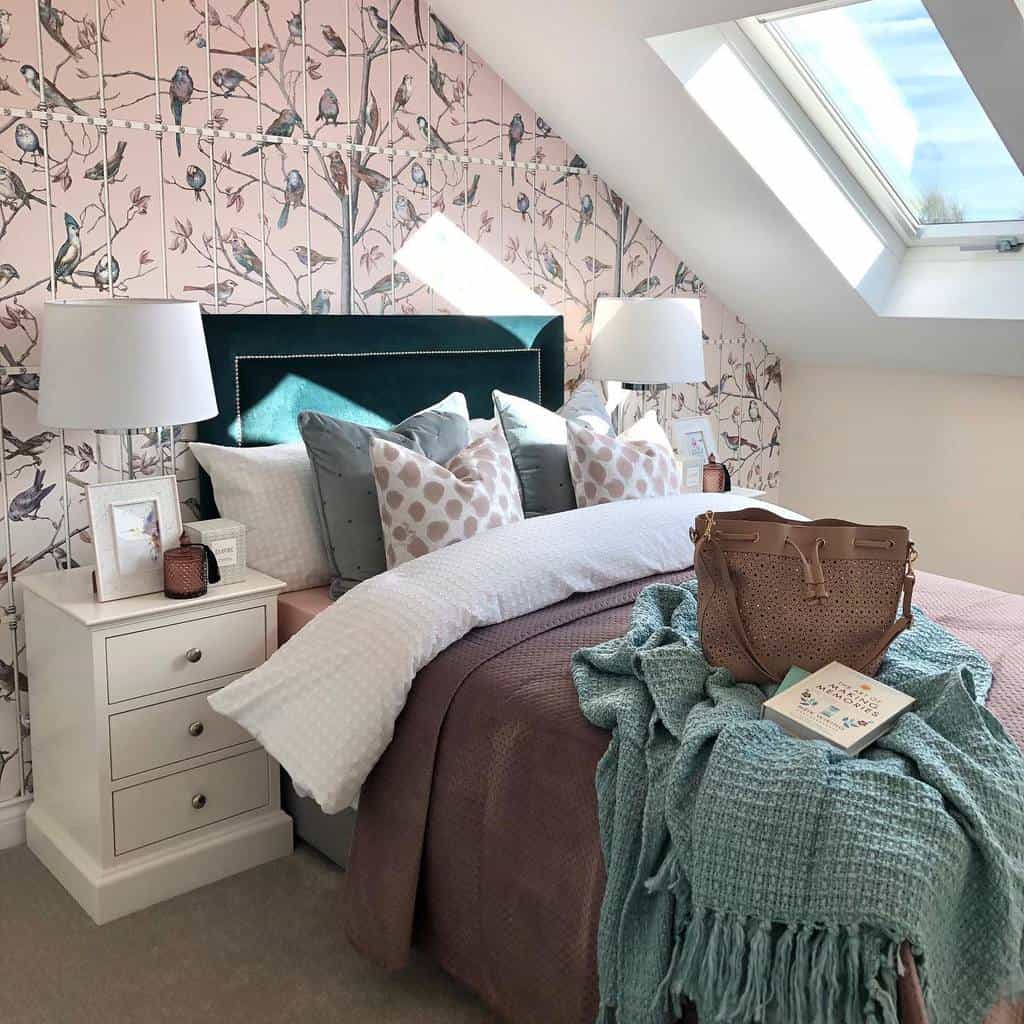 Attic bedroom with pink bird wallpaper, velvet headboard, and cozy bedding under skylight.