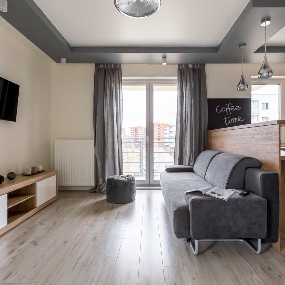 Cozy minimalist living room with a gray sofa, light wooden flooring, and a small 'Coffee Time' nook for a relaxed apartment vibe