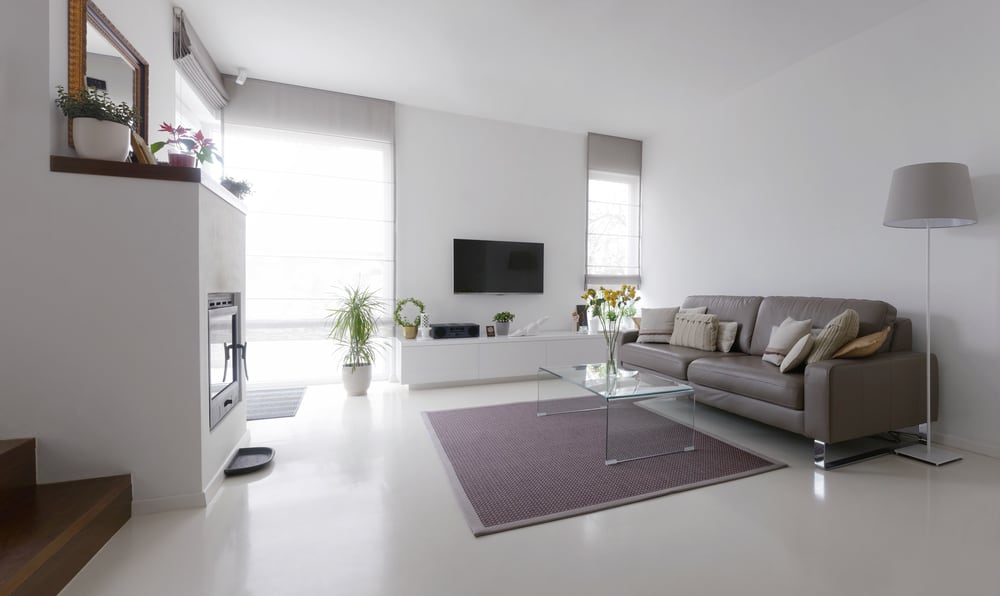 Bright living room with a taupe leather sofa, glass coffee table, and cozy decor featuring plants and a modern fireplace