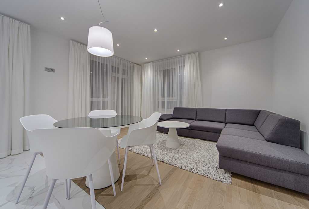 Modern living room featuring a sleek gray sectional sofa, round dining table with white chairs, and soft ambient lighting