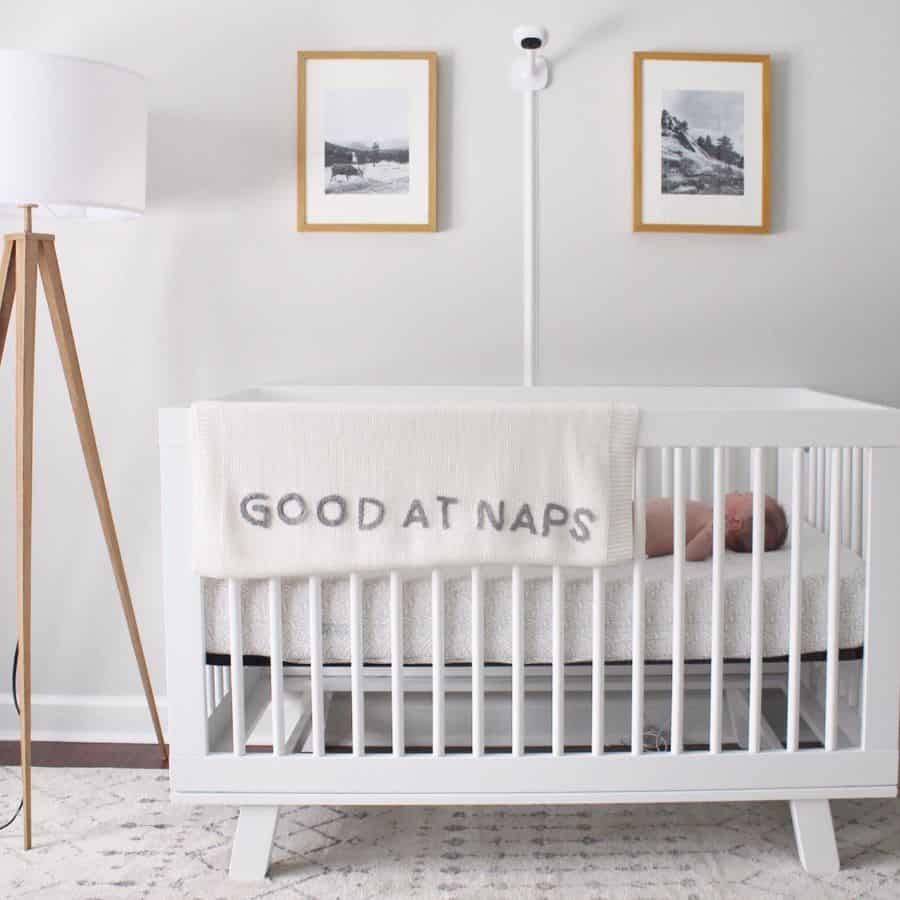 Minimalist baby room with white crib, floor lamp, and "Good at Naps" blanket.