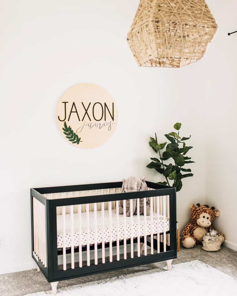 Simple baby room with black crib, personalized name sign, stuffed giraffe, and natural decor accents.