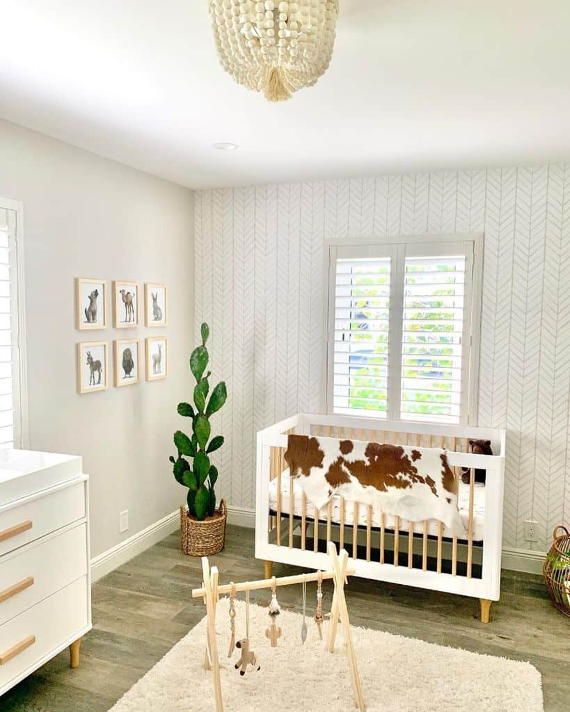 Western-themed baby room with cowhide decor, white crib, animal wall art, and cactus plant.