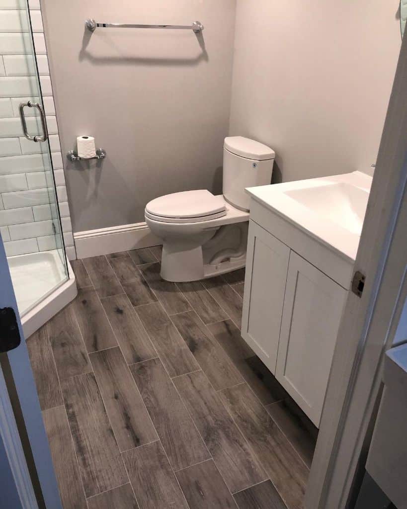 Small white bathroom with wood-look laminate flooring, corner shower, and modern vanity.