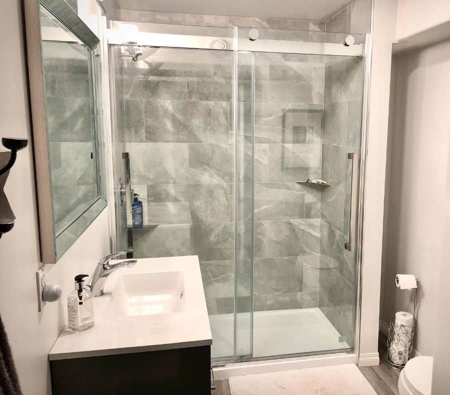 Basement bathroom with marble-tiled shower, glass door, and small modern vanity.