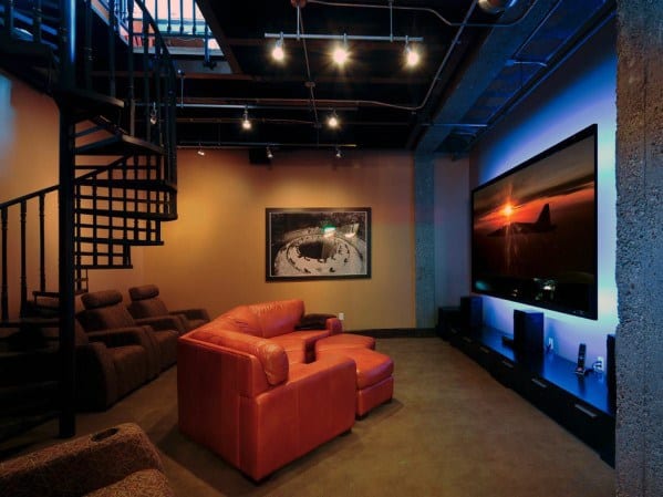 Industrial-style home theater with leather recliners, spiral staircase, and large screen.