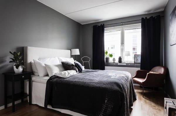 Minimalist bedroom with black curtains, cozy bedding, and natural light from large windows.