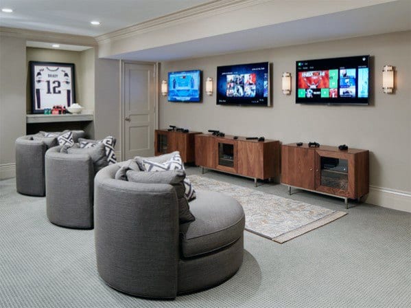 Modern gaming room with three wall-mounted screens, gray circular chairs, and a framed jersey displayed on the wall