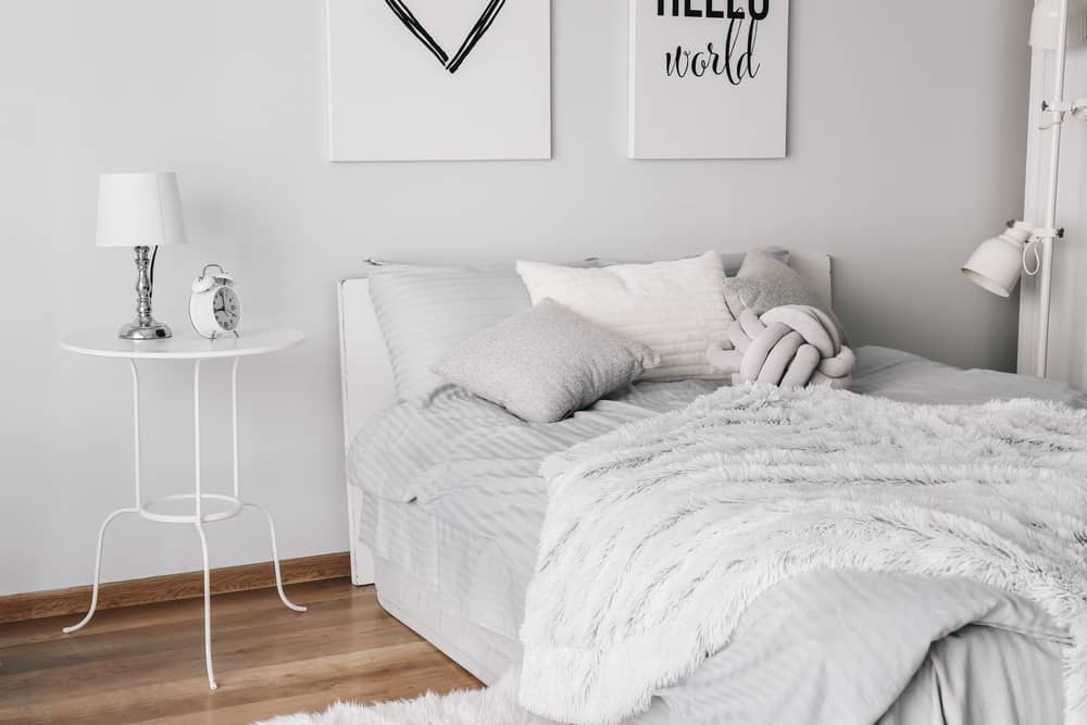 Cozy bedroom with a white bed, fluffy blankets, pillows, and a round side table under soft white light