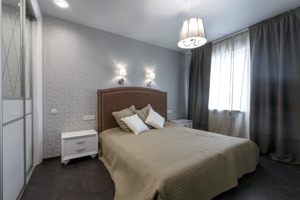 Modern bedroom with textured gray wallpaper, brown curtains, and white bedside dressers.