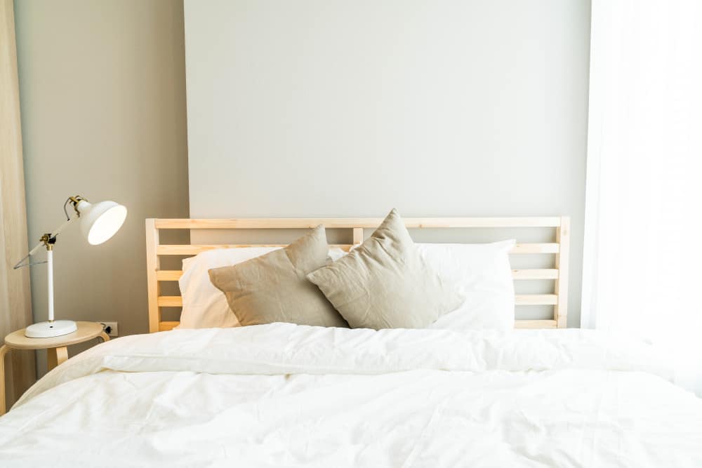 Minimalist bedroom with queen bed, neutral bedding, and a white table lamp.