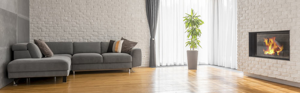 Minimalist living room with a gray sectional sofa, white brick walls, a cozy fireplace, and a vibrant green potted plant