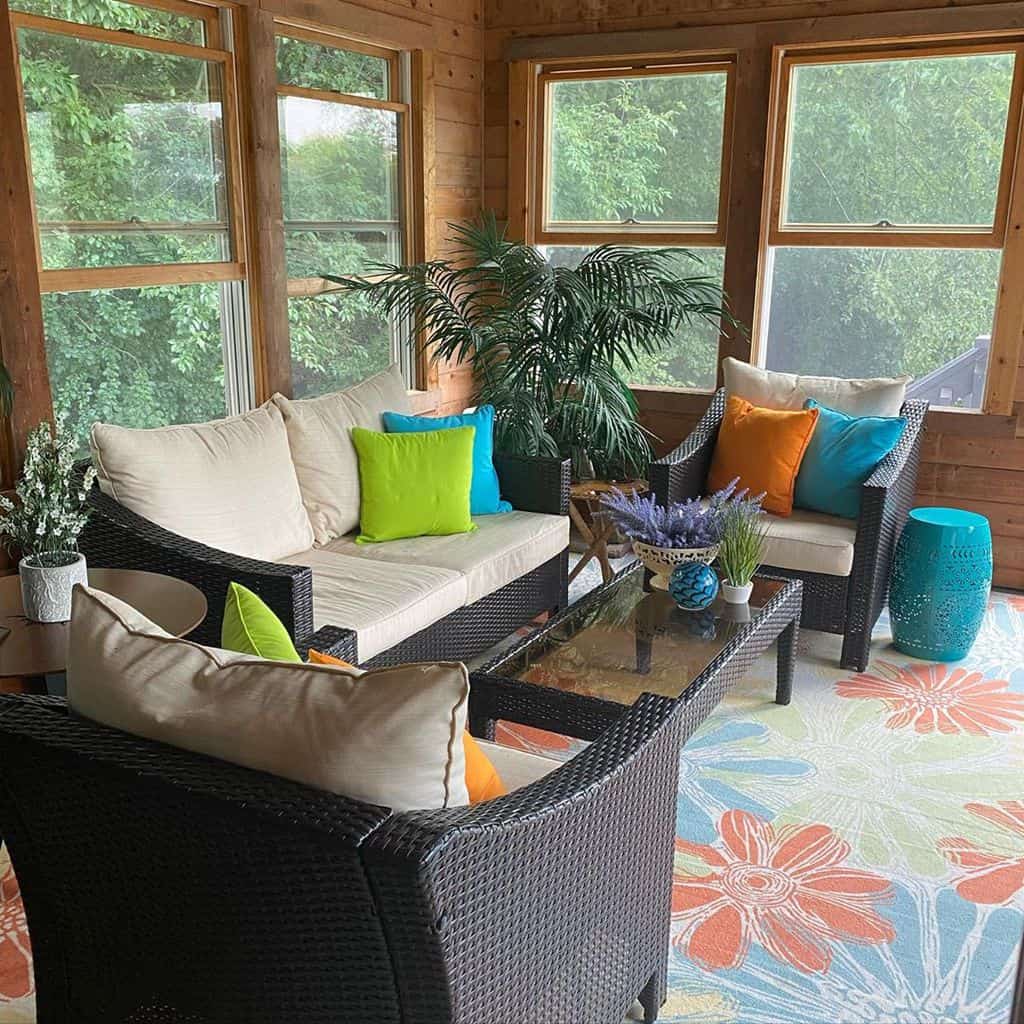 Vibrant sunroom with wicker furniture, colorful pillows, potted plants, and floral area rug.