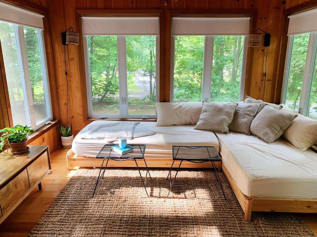 Rustic sunroom with wooden walls, cozy daybed, neutral pillows, and natural light.