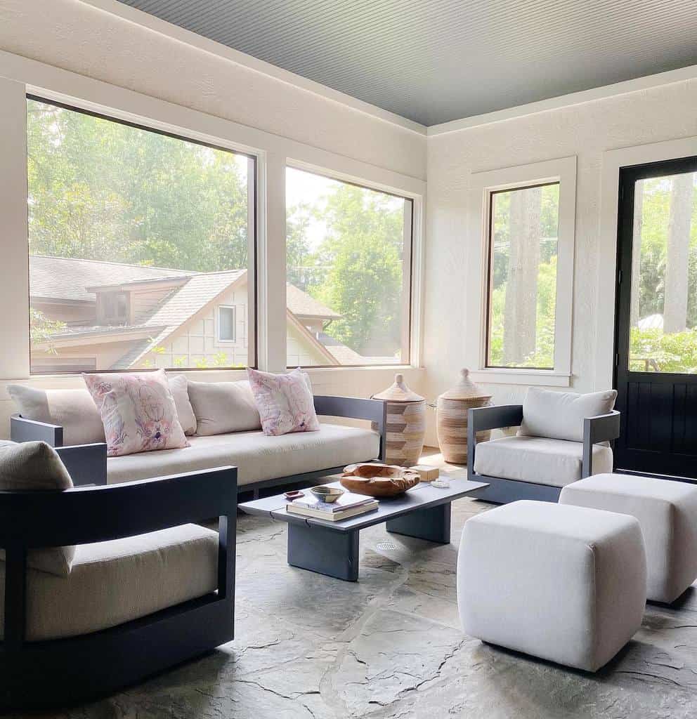 Modern sunroom with sleek furniture, neutral cushions, stone flooring, and minimalist decor.