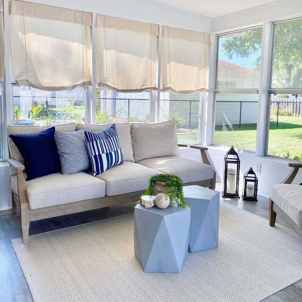 Bright sunroom with beige sofa, blue accent pillows, geometric tables, and neutral decor.