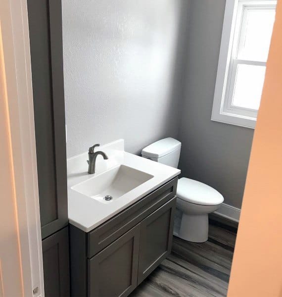 A modern half bath with a sleek sink, gray vanity, white toilet, window, and wood-patterned flooring