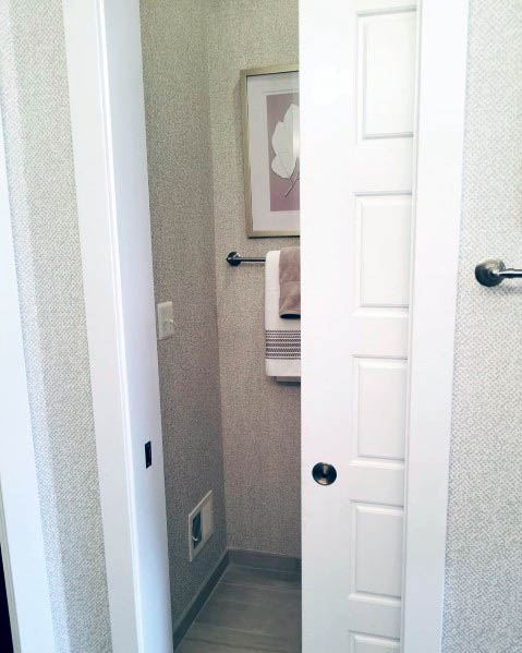 White pocket door with classic panel design leads to a small half-bathroom featuring neutral wallpaper, towel rack, and framed artwork