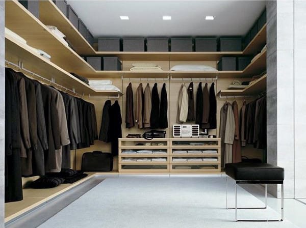 Modern walk-in closet with hanging suits, shelves with clothes, and storage boxes; minimalist design