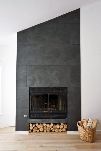 A striking fireplace design with dark slate tiles, an asymmetrical layout, and wood storage underneath for a modern rustic look.