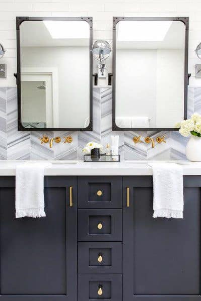 Bathroom with herringbone tile backsplash, dark grey vanity, and gold fixtures.