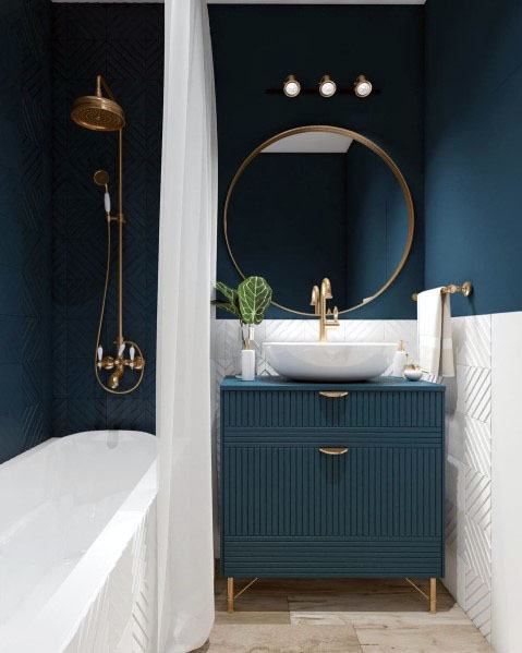 Small modern bathroom with blue vanity, round mirror, and gold fixtures.