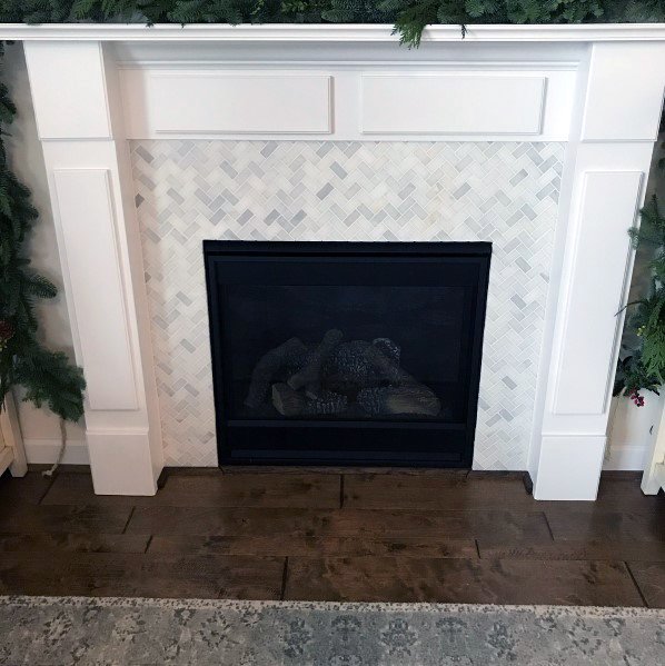 Fireplace with white herringbone tile surround, black gas insert, and white wooden mantel.