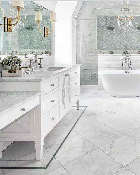 Luxury white bathroom with freestanding tub, marble flooring, and crystal chandelier.