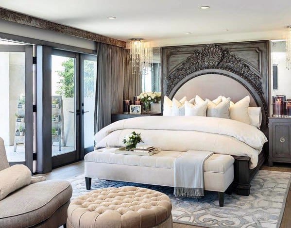 Spacious bedroom with ornate wood headboard, plush bedding, and tufted ottoman.