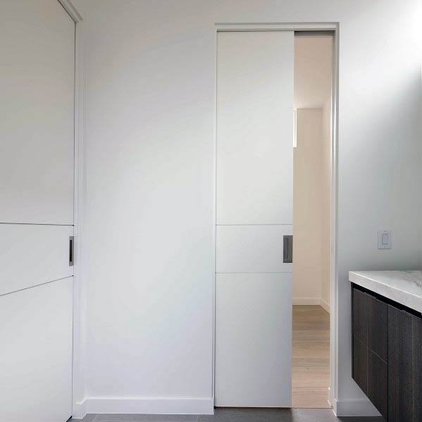 Minimalist white pocket door with a modern handle leads to a sleek bathroom featuring clean lines and neutral tones