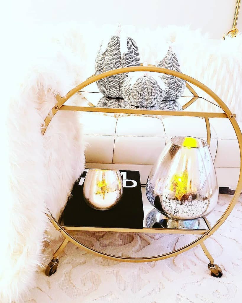 Circular gold bar cart with metallic decor, candles, and plush pumpkins on mirrored shelves.